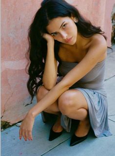 Woman with long dark hair in a strapless dress squatting outdoors