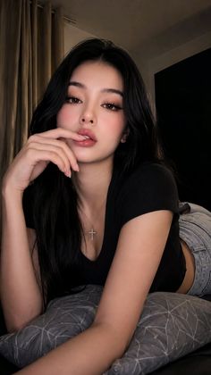 Woman with long black hair in a black t-shirt and jeans, lying on a pillow