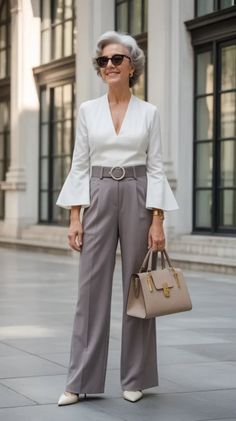 Woman in a white blouse and grey wide-leg pants holding a handbag outdoors