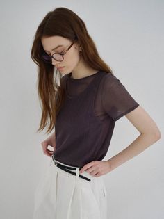 Woman with long hair and glasses wearing a sheer top and white pants