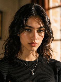 Woman with long wavy hair wearing a black sweater and silver necklace