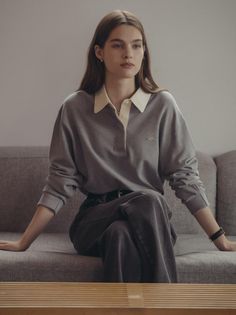 Woman with long hair wearing a gray polo shirt and jeans, sitting on a sofa