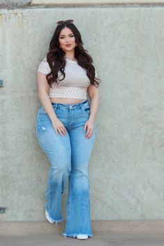 Woman with long hair wearing a crop top and flared jeans leaning against a wall