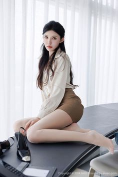 Woman with long black hair wearing a white shirt and brown shorts, kneeling indoors