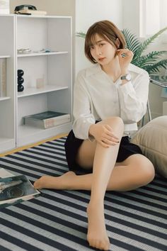 Woman with short hair wearing a white shirt and black skirt, sitting on a striped rug