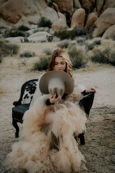 Woman in a tulle dress and cowboy hat sitting in a desert landscape