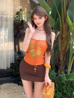 Woman in an orange tube top and brown mini skirt winking outdoors