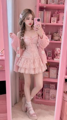 Woman in a pink lace dress and cardigan taking a mirror selfie in a pink room