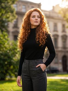 Woman with long red curly hair in a black turtleneck and grey pants outdoors