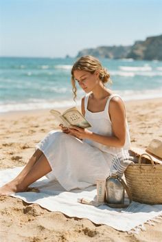 Woman in a white dress reading a book on a sunny beach