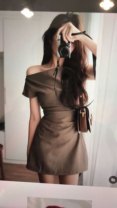 Woman in a brown off-shoulder dress taking a mirror selfie with a camera