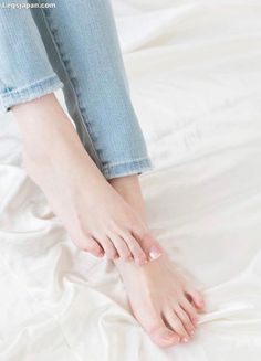 Bare feet with a light pedicure on white bedding, wearing light wash jeans