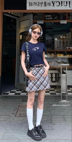 Woman in a plaid skirt and crop top with pigtails and headphones outdoors
