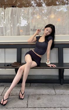 Woman with long black hair wearing a crop top and mini skirt sitting on a bench