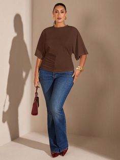 Woman in a brown top and blue jeans holding a red handbag indoors