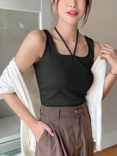 Woman in a black tank top and brown pants with a white shirt draped over her shoulders