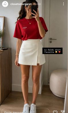 Woman in a red t-shirt and white skirt taking a mirror selfie indoors