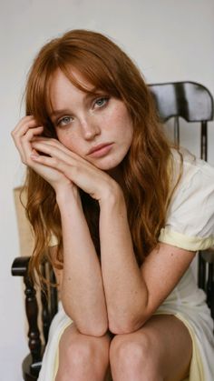 Woman with red hair and freckles in a white dress sitting indoors