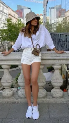 Woman in a bucket hat, white shirt, and shorts standing on a bridge in a city