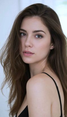 Woman with long brown hair wearing a black top, looking over her shoulder