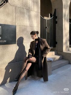 Woman in a long coat and black tights sitting outdoors in sunlight