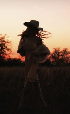 Woman in a cowboy hat and dress in a field at golden hour