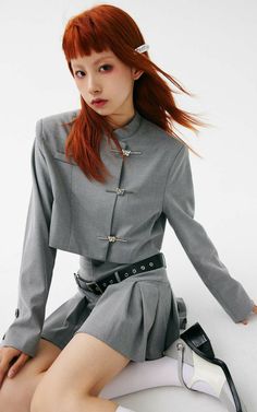 Woman with red hair in a gray cropped jacket and pleated skirt