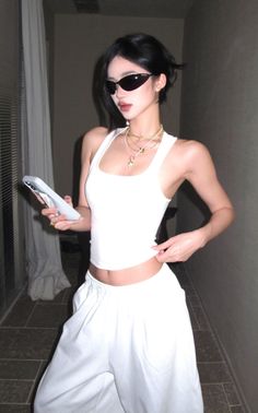Woman in a white tank top and sunglasses holding a phone indoors