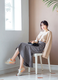 Woman in a plaid skirt and beige sweater sitting on a chair indoors