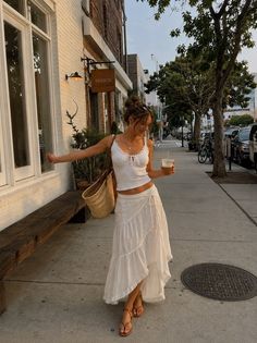 Woman in a white crop top and long skirt walking on a street at golden hour
