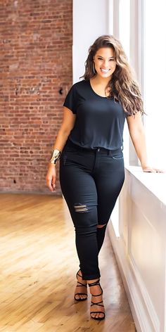 Woman in black t-shirt and ripped jeans with long wavy hair, smiling indoors