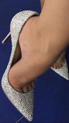 Foot in a rhinestone high heel with a red sole against a blue background