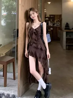 Woman in a brown ruffle dress and platform shoes leaning against a wooden door