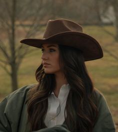 Woman in a cowboy hat and green jacket looking to the side outdoors