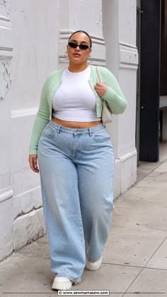 Woman with a curvy body wearing a light green cardigan and wide leg jeans on a street