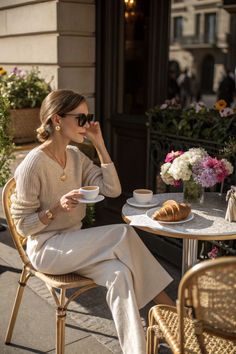 Woman in sunglasses and a sweater enjoying coffee and a croissant at an outdoor cafe