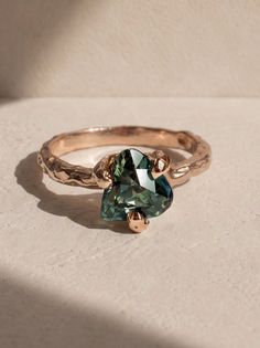 Rose gold ring with a green gemstone and textured band under natural light