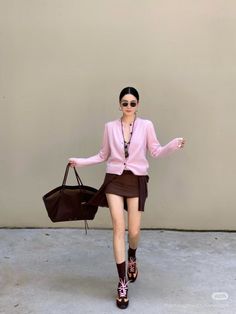 Woman in a pink cardigan and brown mini skirt with a tote bag and sunglasses