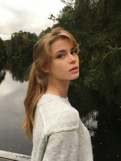 Woman with blonde hair in a grey sweater by a lake on an overcast day