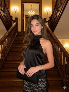 Woman in a black top and lace skirt holding a clutch bag on a grand staircase