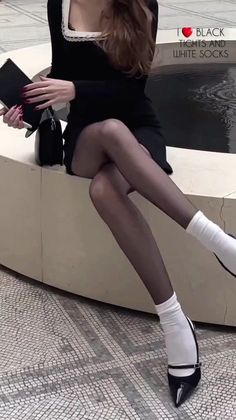 Woman in a black dress, black tights, and white socks sitting indoors