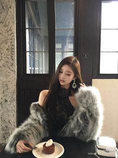 Woman with long hair wearing a fur coat and black lace top, eating dessert indoors