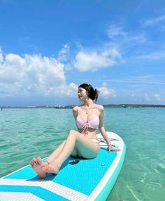 Woman in a pink bikini sitting on a paddleboard in clear blue water