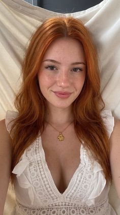 Woman with red hair and freckles wearing a white dress and gold necklace