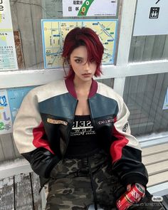 Person with red hair wearing a bomber jacket and camo pants in an urban setting