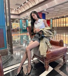 Woman in a white shirt and mini skirt sitting on a leather chair indoors