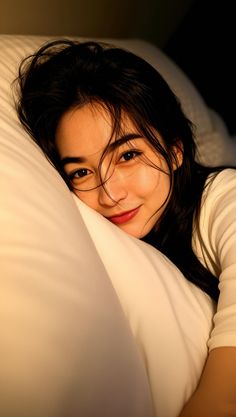 Woman with long dark hair smiling while lying on a pillow in bed
