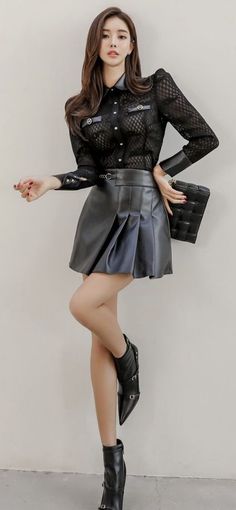 Woman in a black sheer shirt and leather skirt posing indoors