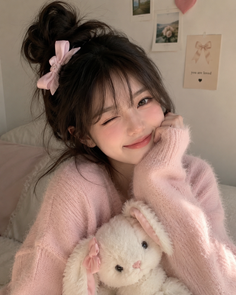 Woman in a pink sweater with a messy bun and a stuffed bunny, winking