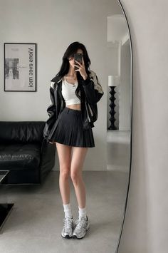 Woman in a crop top and pleated skirt taking a mirror selfie indoors